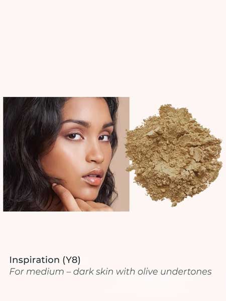 A woman with medium-dark skin and olive undertones poses beside INIKA Organic Loose Mineral Foundation SPF25 8g in Inspiration (Y8), ideal for medium-dark skin with olive undertones.