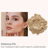 A woman with medium skin touches her face next to a pile of beige INIKA Organic Loose Mineral Foundation SPF25 8g, shade Patience (Y5), for medium skin with warm undertones.
