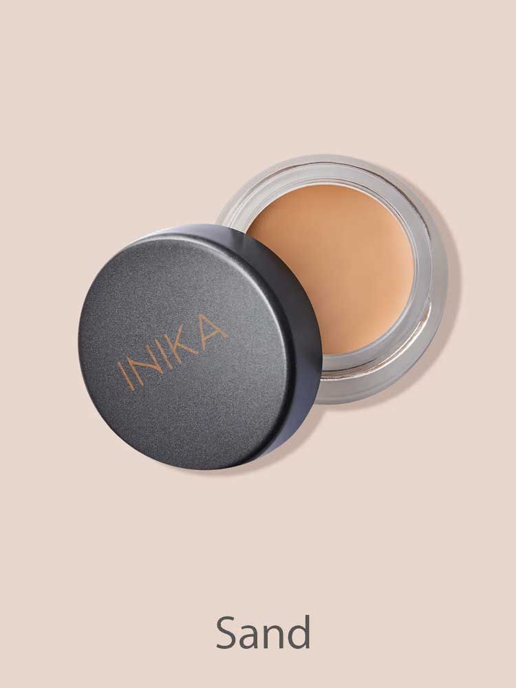 An open INIKA Organic Full Coverage Concealer 3.5g in Sand displays its smooth, light beige shade. The black lid shows the INIKA logo, with Sand labeled below—ideal for flawless, full coverage.