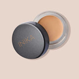 An open INIKA Organic Full Coverage Concealer 3.5g in Sand displays its smooth, light beige shade. The black lid shows the INIKA logo, with Sand labeled below—ideal for flawless, full coverage.