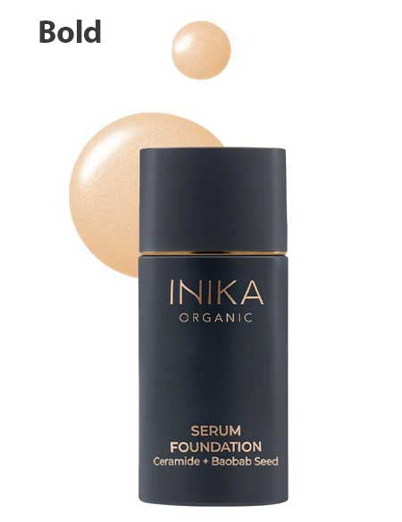 A black bottle of INIKA Organic Serum Foundation 25ml, a hydrating and anti-ageing makeup with Ceramide and Baobab Seed, labeled Bold. Beige foundation swatches appear in the background.