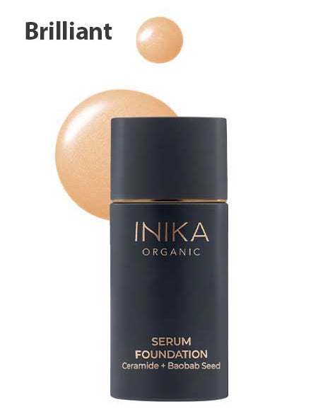 A black bottle labeled INIKA Organic Serum Foundation 25ml stands before a glowing beige swatch, with "Brilliant" above—this hydrating foundation blends anti-ageing benefits and radiant coverage.