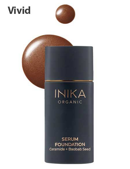 A bottle of INIKA Organic Serum Foundation 25ml, a hydrating foundation with Ceramide and Baobab Seed, is placed in front of two drops of brown liquid foundation on a white background. "Vivid" appears in bold at the top left.
