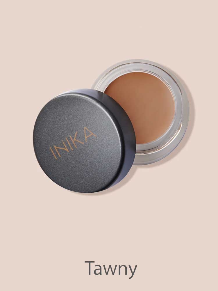 An open INIKA Organic Full Coverage Concealer 3.5g in the Tawny shade sits with its lid beside it on a beige background. "Tawny" is written below the image.