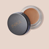 An open INIKA Organic Full Coverage Concealer 3.5g in the Tawny shade sits with its lid beside it on a beige background. "Tawny" is written below the image.