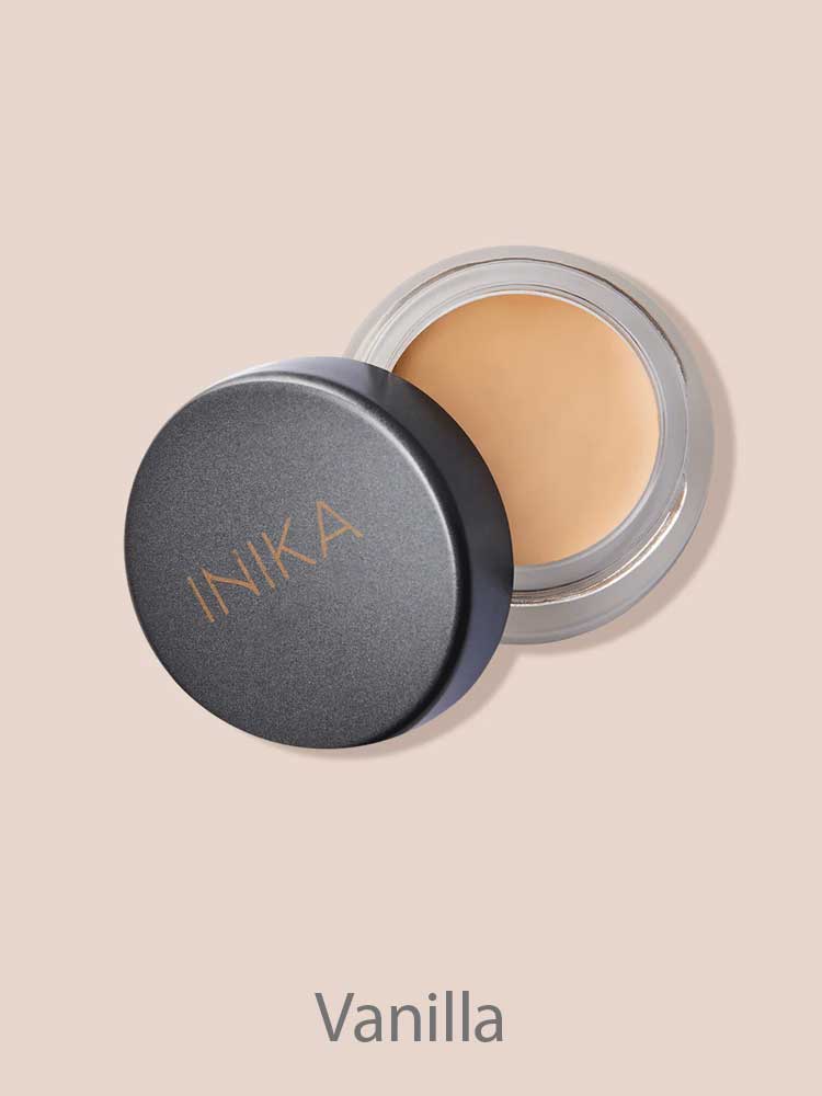 An open INIKA Organic Full Coverage Concealer 3.5g in Vanilla, lid set aside to show the creamy formula inside, rests on a beige background.