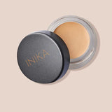 An open INIKA Organic Full Coverage Concealer 3.5g in Vanilla, lid set aside to show the creamy formula inside, rests on a beige background.