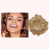 A smiling woman with curly hair is pictured next to a pile of INIKA Organic Loose Mineral Foundation SPF25 8g against a light background.
