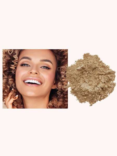 A smiling woman with curly hair is pictured next to a pile of INIKA Organic Loose Mineral Foundation SPF25 8g against a light background.