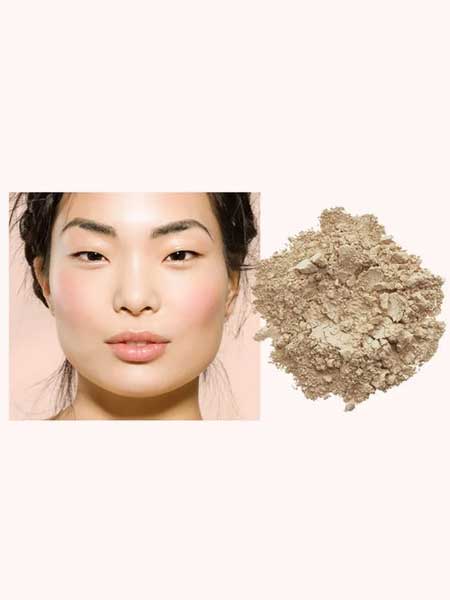 A woman with smooth, glowing skin and soft pink blush sits beside INIKA Organic Loose Mineral Foundation SPF25 8g, displayed as a loose powder on a light background.