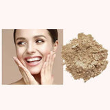A smiling woman touches her face with both hands beside a pile of INIKA Organic Loose Mineral Foundation SPF25 8g, featuring light beige organic powder on a plain background.