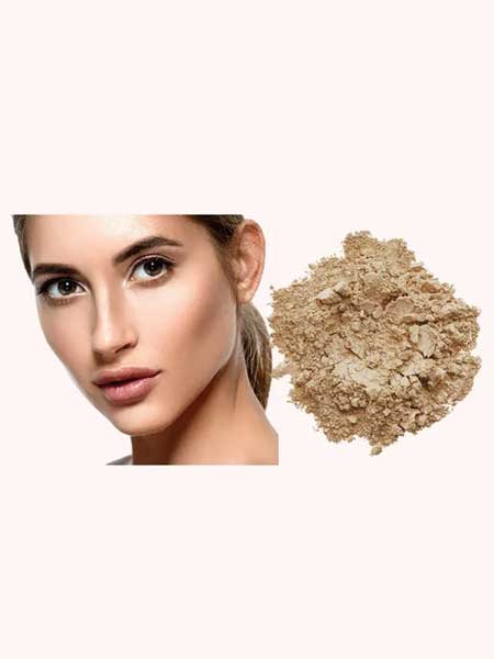 A woman with clear skin and neutral makeup looks forward; next to her is a pile of INIKA Organic Loose Mineral Foundation SPF25 8g on a white background.