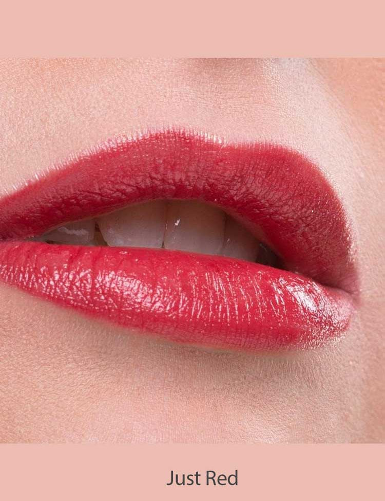 A close-up of lips wearing Benecos Natural Lipsticks 4.5g in glossy red, slightly parted to reveal white teeth. The background is soft pink with "Just Red" text at the bottom.