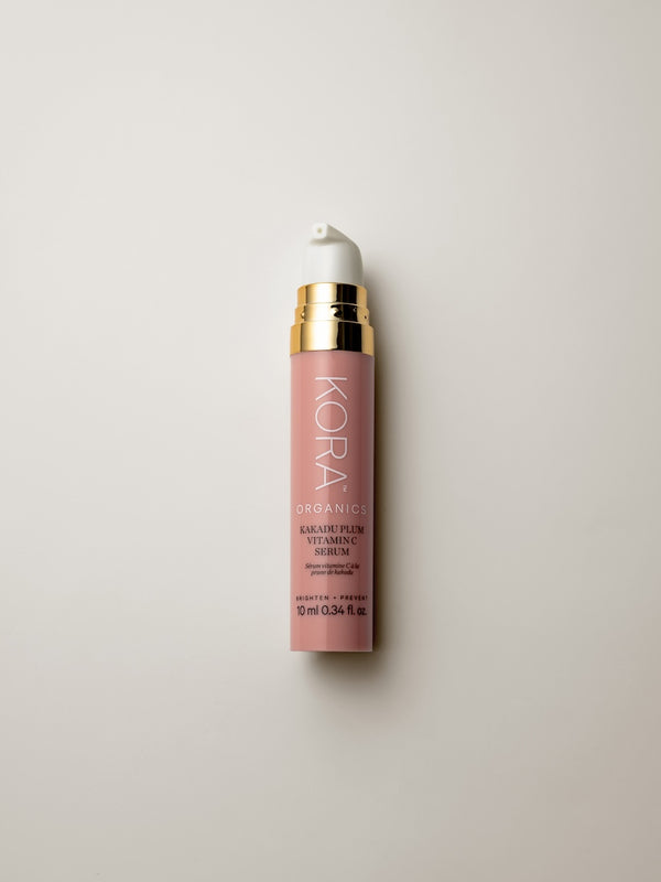 Small dusty-pink 10 ml KORA Kakadu Plum Vitamin C Serum bottle with a white pump and gold collar, lying on a warm grey surface.