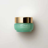 A small, round, light green jar with a shiny gold lid labeled “KORA Organics Active Algae Lightweight Moisturiser” rests on a white background—ideal for those with oily or combination skin seeking lightweight hydration.