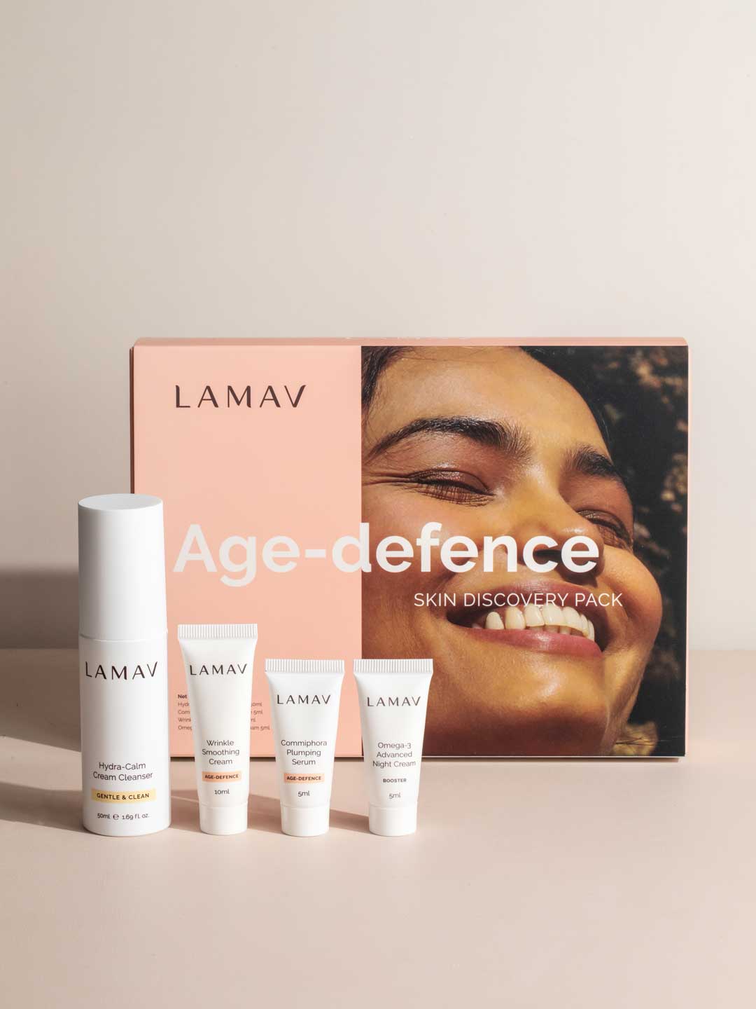The LAMAV Age-Defence Skin Discovery Pack (4 Pack) is displayed in front of its box, featuring a smiling face—ideal for those seeking organic, anti-ageing skincare from LAMAV.