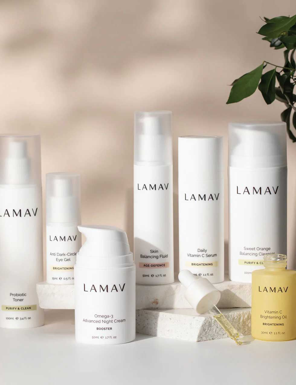 The LAMAV Age-Defence Complete Skincare Collection for Oily/Combination Skin (7 pack) is displayed on a white surface, accented with a leafy branch and natural stones for a touch of greenery and texture.