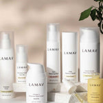 The LAMAV Age-Defence Complete Skincare Collection for Oily/Combination Skin (7 pack) is displayed on a white surface, accented with a leafy branch and natural stones for a touch of greenery and texture.