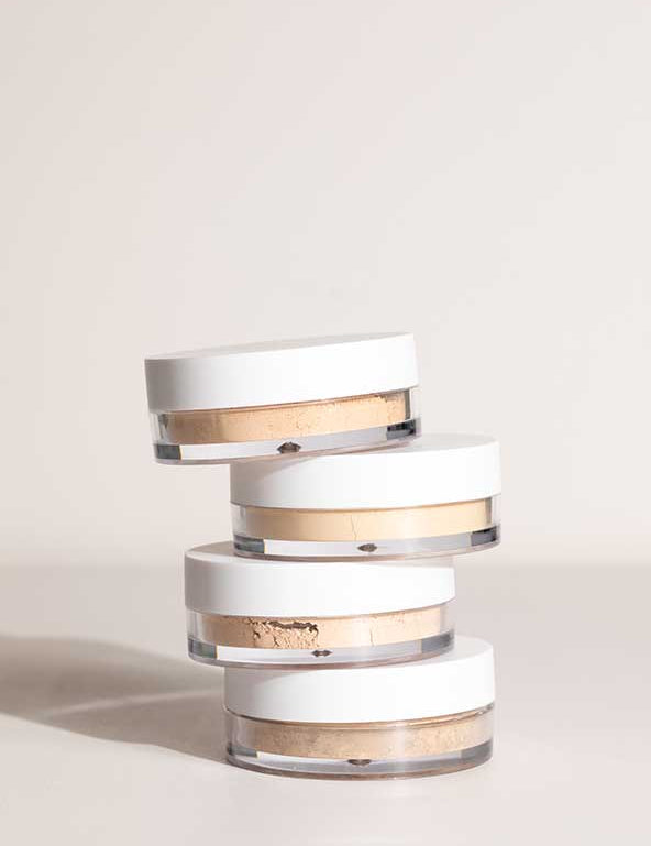Four round LAMAV Anti Ageing Mineral Foundation SPF 15 containers with white lids are stacked unevenly atop one another against a neutral background.
