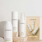 Three LAMAV skincare products from the Brightening Skin Discovery Pack are displayed with minimalist white packaging on a neutral background accented by stone props. A box labeled "Organic Skincare Essentials" features the LAMAV brand.