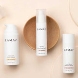 Three LAMAV Age-Defence Skin Discovery Pack bottles are arranged on a beige background—one on a brown dish in the center, with two others beside it. This 3-pack offers an organic vegan skincare routine ideal for anti-ageing.