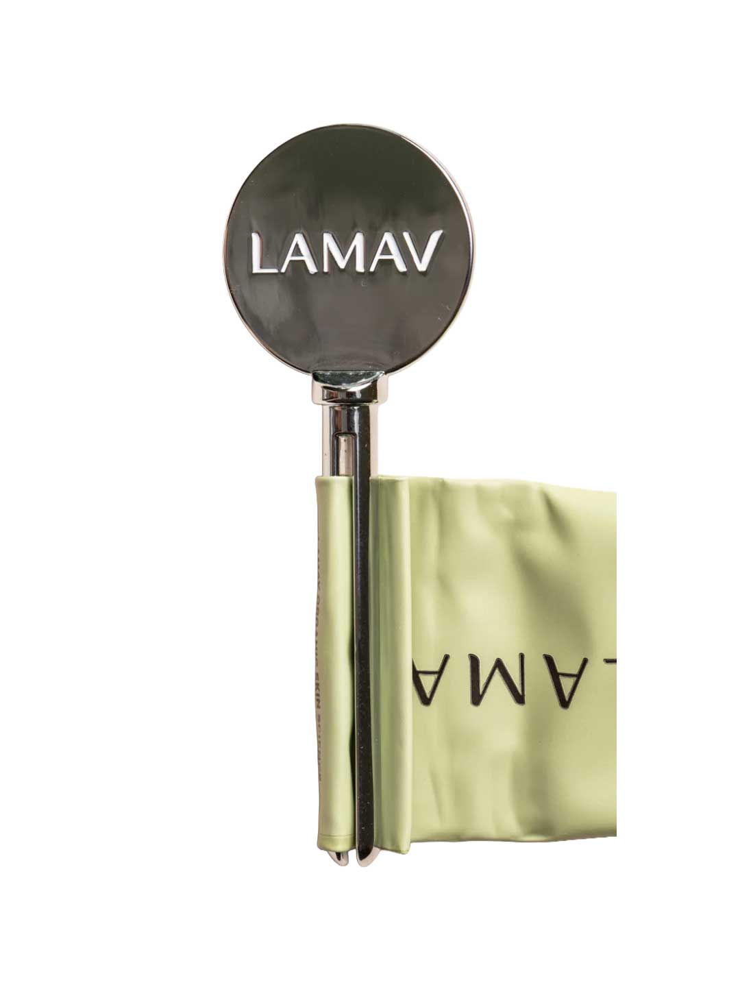 The LAMAV Tube Key—a shiny, round metal tool engraved with LAMAV—hangs from a pale green, folded fabric band featuring the logo, presented as a zero-waste beauty solution on a crisp white background.