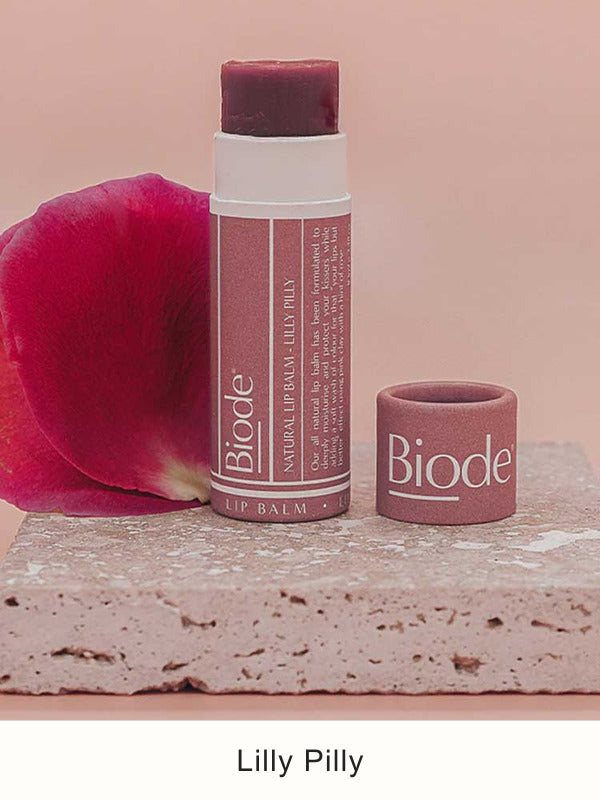 Uncapped Biode Lilly Pilly balm with a deep plum-coloured stick and rose-pink paper tube on pink stone, beside its cap and a rose petal. Lilly Pilly is printed below.