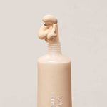 A beige tube of Ere Perez Lychee Crème Corrector 10ml with the cap off reveals a swirl of creamy, hydrating under-eye corrector emerging from the nozzle against a simple light background.