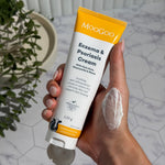 Hand holding an open white-and-yellow MooGoo Eczema and Psoriasis Cream tube marked 120g, with a thick white smear on the back of the hand.