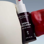 A 30ml bottle of Madara Derma Collagen Peptide Serum is held between a white surface and a shiny red object, set against a light blue background. The dark bottle features white text and a white pump.
