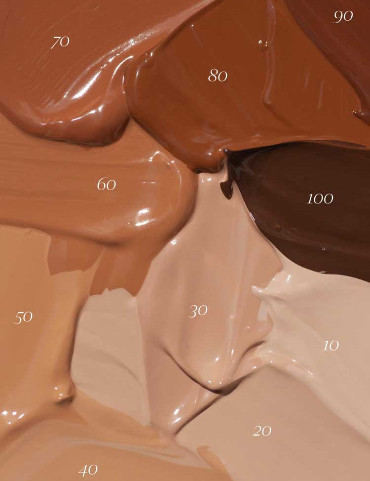 Thick swatches of Madara Skin Equal Soft Glow Foundation SPF15 30ml in shades 10 to 100 are arranged in a textured, overlapping display, highlighting the product’s diverse range of skin tone options.