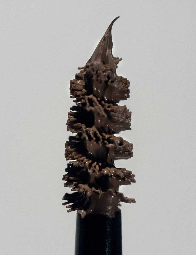 Close-up of a mascara wand coated in brown mascara, ideal for fuller, defined lashes and brows. Pair with Madara Grow & Fix Tinted Brow Gel 4.25ml for a polished look against a plain light background.