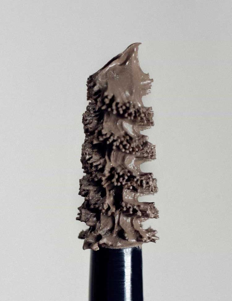 A close-up of the Madara Grow & Fix Tinted Brow Gel 4.25ml wand, coated with light brown product, showcases its textured bristles and detail against a plain light background.
