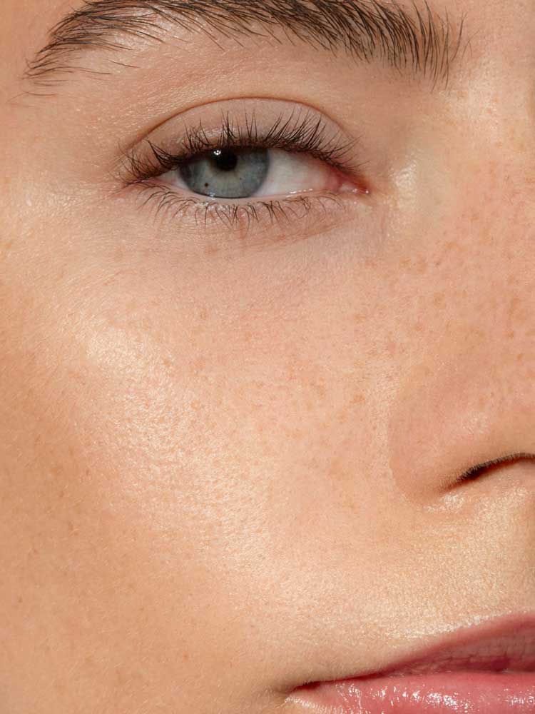 Close-up of a person's face with one blue eye, eyebrow, upper cheek, nose, and part of the mouth. Skin looks smooth with visible freckles and a natural complexion, enhanced by Madara H2O Tint Hyaluron Tinted Serum 30ml.