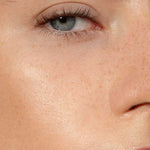 Close-up of a person's face with one blue eye, eyebrow, upper cheek, nose, and part of the mouth. Skin looks smooth with visible freckles and a natural complexion, enhanced by Madara H2O Tint Hyaluron Tinted Serum 30ml.