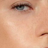 Close-up of a person's face with one blue eye, eyebrow, upper cheek, nose, and part of the mouth. Skin looks smooth with visible freckles and a natural complexion, enhanced by Madara H2O Tint Hyaluron Tinted Serum 30ml.