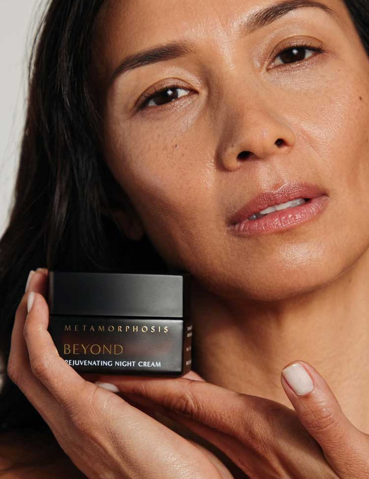 A woman with smooth, glowing skin holds the Metamorphosis Beyond Rejuvenating Night Cream 50ml near her face, highlighting this bakuchiol cream specially formulated to nourish and rejuvenate menopausal skin.