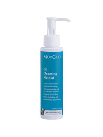 A white pump bottle labeled MooGoo Oil Cleansing Method 100ml sits against a blue backdrop, described as a rich blend of oils ideal for all skin types. The 100ml (3.38 fl oz) product uses the oil cleansing method for gentle cleansing.