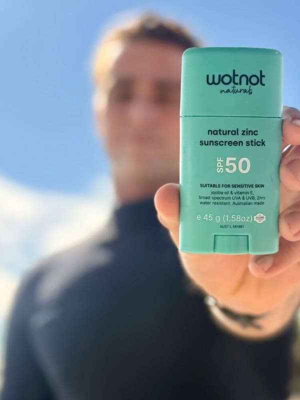 Man holding Wotnot Natural Zinc Sunscreen Stick SPF 50 at the beach