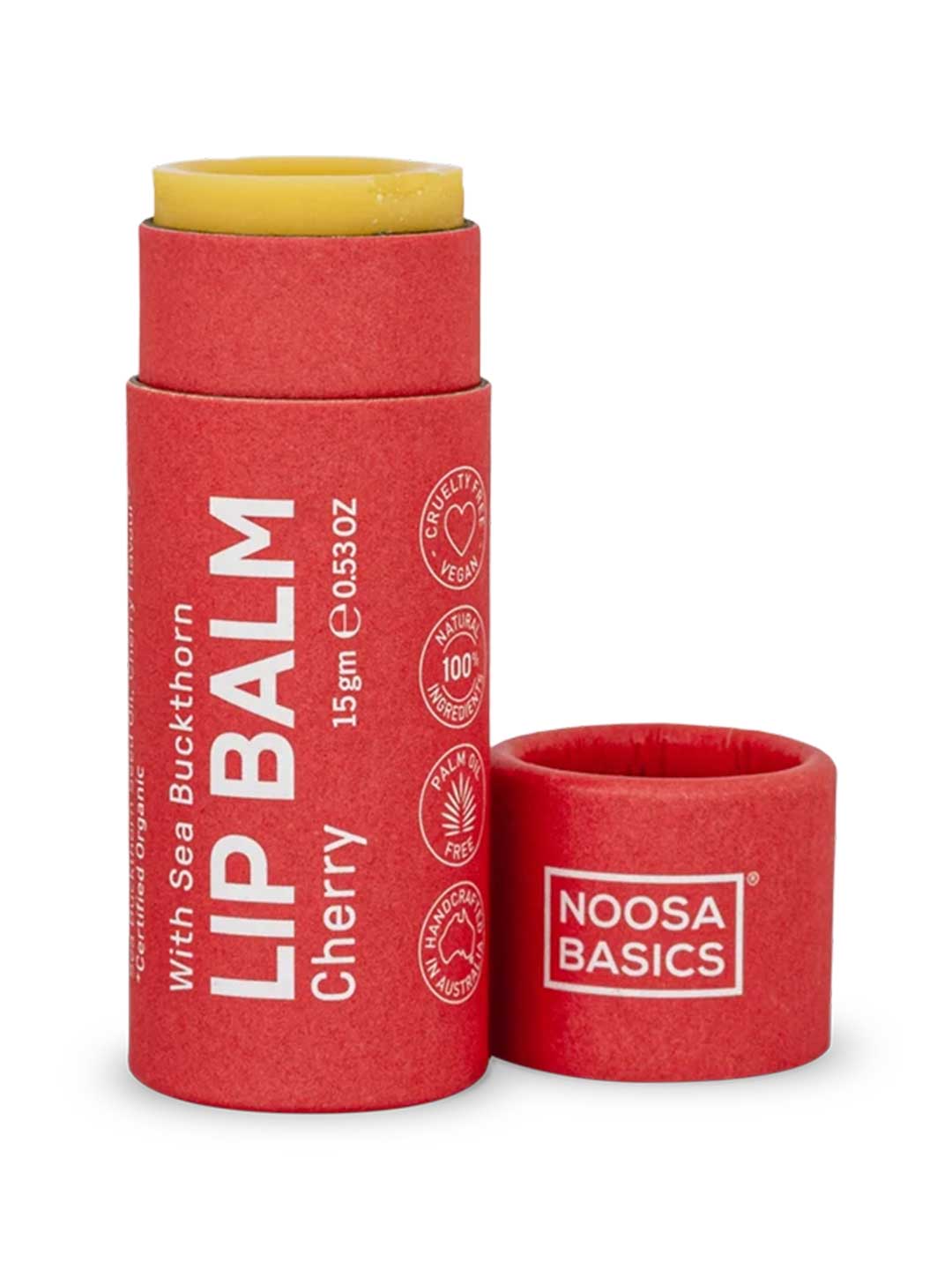 Noosa Basics Cherry lip balm in a red paper tube with a yellow balm stick visible at the top, shown with the cap removed on a white background.