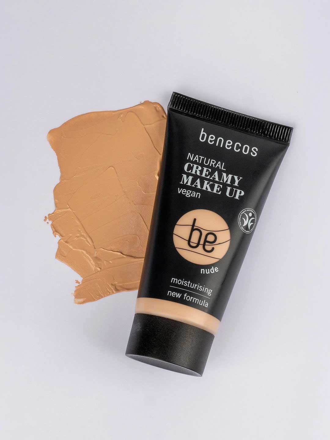 A 30ml tube of Benecos Natural Creamy Makeup sits on a white surface next to a smear of beige cream. The vegan, moisturising formula helps achieve a flawless finish.