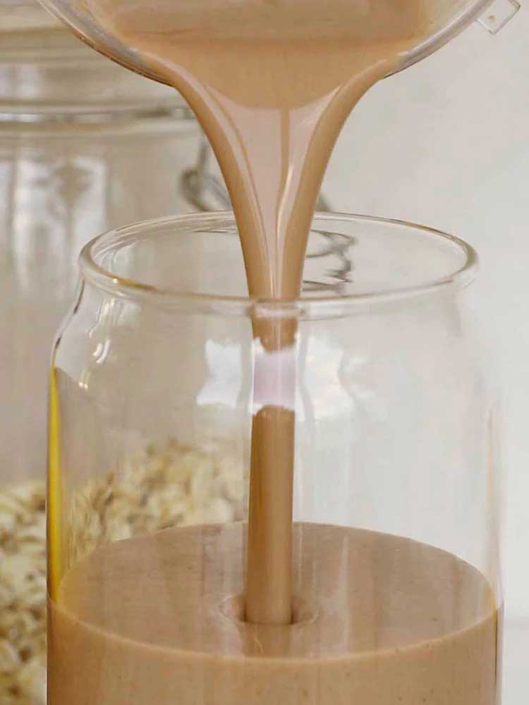 Nutra Naturals Collagen Protein Unflavoured, a creamy light brown liquid, is poured into a clear glass jar with rolled oats in the background—ideal for muscle recovery thanks to added collagen protein.
