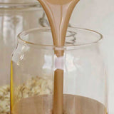 Nutra Naturals Collagen Protein Unflavoured, a creamy light brown liquid, is poured into a clear glass jar with rolled oats in the background—ideal for muscle recovery thanks to added collagen protein.