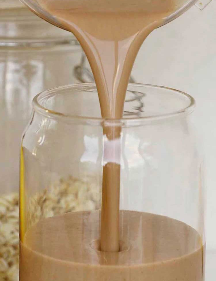 Nutra Naturals Collagen Protein Unflavoured, a creamy light brown liquid, is poured into a clear glass jar with rolled oats in the background, ideal for muscle recovery thanks to added collagen protein.