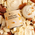 A tin of Nutra Naturals Collagen White Hot Choc Salted Caramel 200g sits among white chocolate chunks, caramel pieces, and a cup finished with whipped cream and caramel bits.