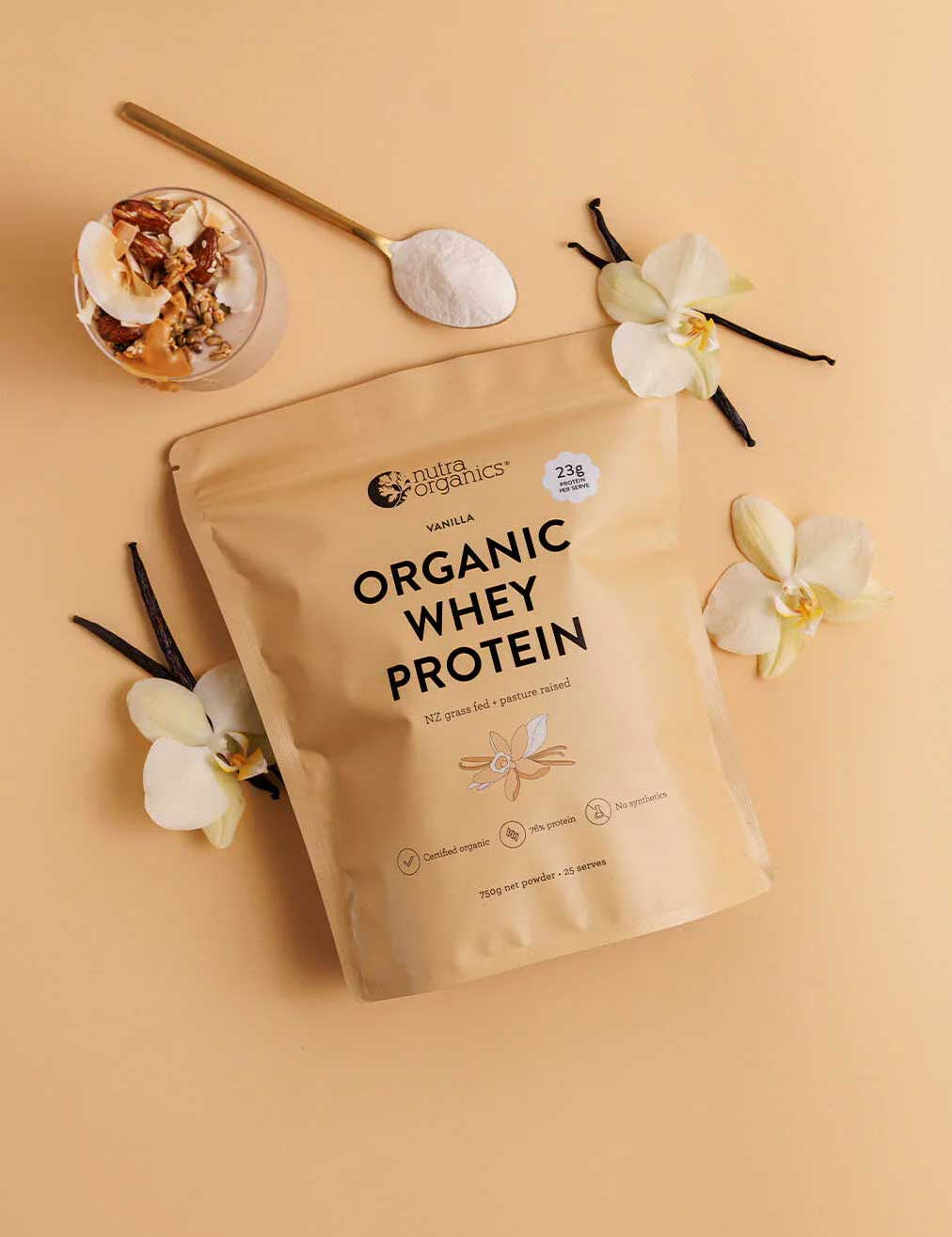 A beige pouch of Nutra Naturals Organic Whey Protein Vanilla 750g, made from grass-fed New Zealand dairy, rests on a light tan surface with white orchids, vanilla beans, a spoon of protein powder, granola, yogurt, and fruit.