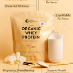A beige pouch of Nutra Naturals Organic Whey Protein Vanilla 750g, made from grass-fed New Zealand dairy, sits beside a glass of milk, vanilla protein powder, a spoon, and white orchids. Text notes it's organic, high in protein/BCAAs, and family-friendly.