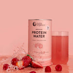 A canister of Nutra Naturals Protein Water Berry Bliss 450g stands beside a glass of the pink drink, surrounded by strawberries, raspberries, and water, all set against a pink background.