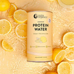 A canister of Nutra Naturals Protein Water Lemonade 450g, rich in electrolytes, is surrounded by sliced and whole lemons plus a glass of lemonade on a textured yellow surface with water splashes.