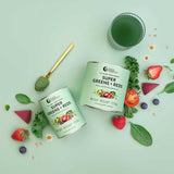 Two containers of Nutra Naturals Super Greens + Reds with a scoop, surrounded by superfoods—leafy greens, strawberries, spinach, blueberries, tomato, and a green drink in a glass—all set on a pale green background.